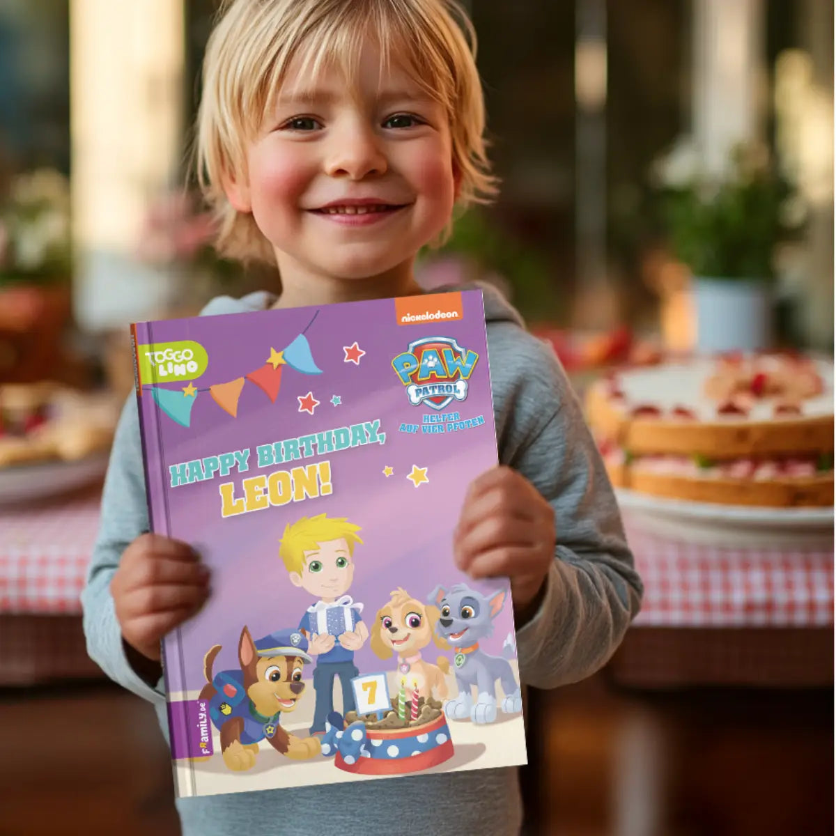 Ein strahlender Junge hält das personalisierte Paw Patrol- Buch "Happy Birthday, Leon!" in die Kamera. Im Hintergrund sieht man einen gedeckten Geburtstagstisch