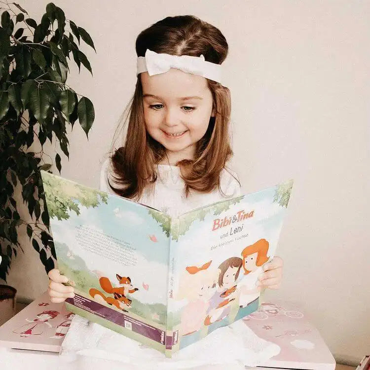Ein MĂ€dchen liest ein Buch von Bibi und Tina