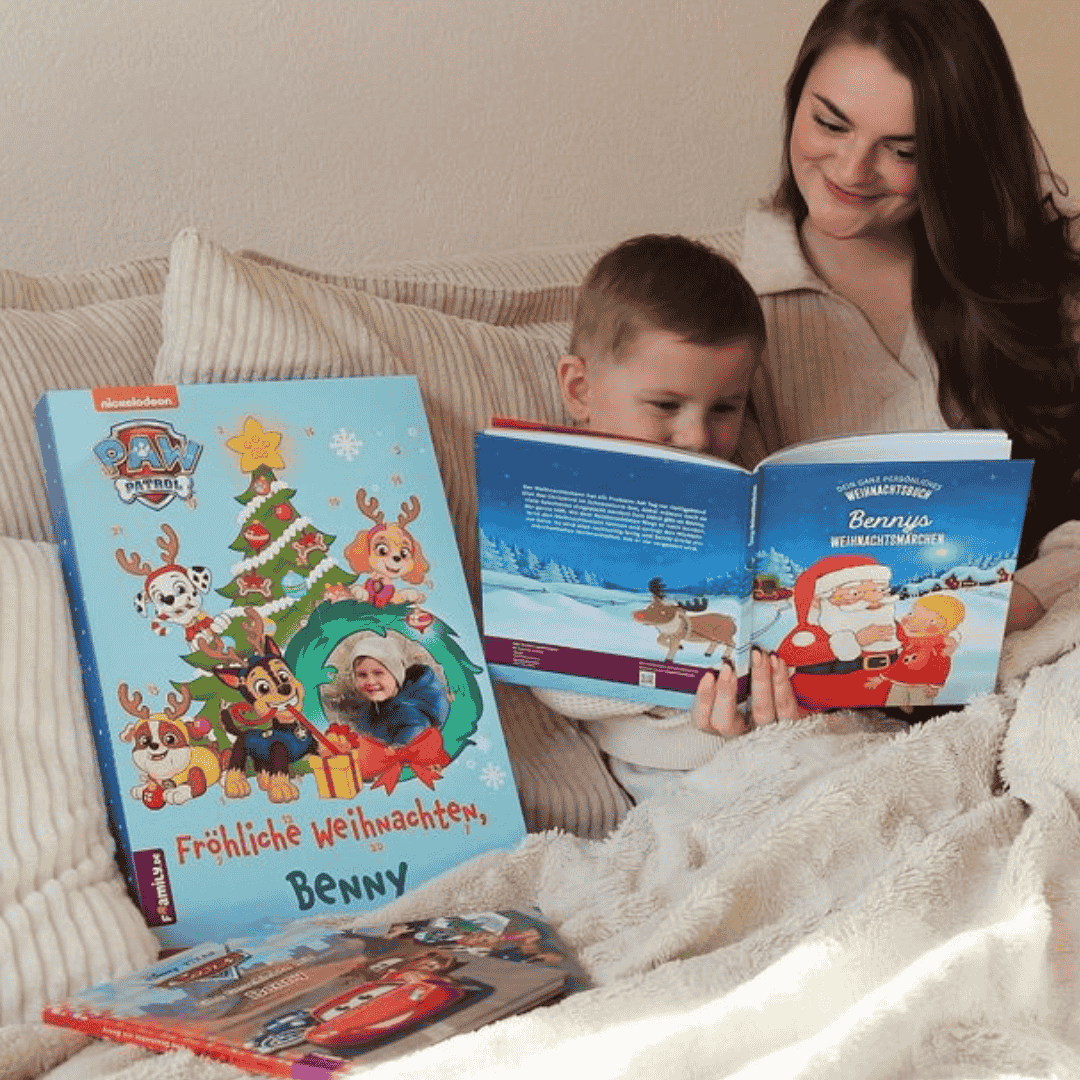 Eine Frau und ein kleiner Junge sitzen zusammen auf einer gemütlichen Decke und lesen festliche Weihnachtsbücher. Ein großes Paw Patrol-Weihnachtsbuch und andere Kindergeschichten sind in der Nähe zu sehen, während sie den fröhlichen Moment genießen.