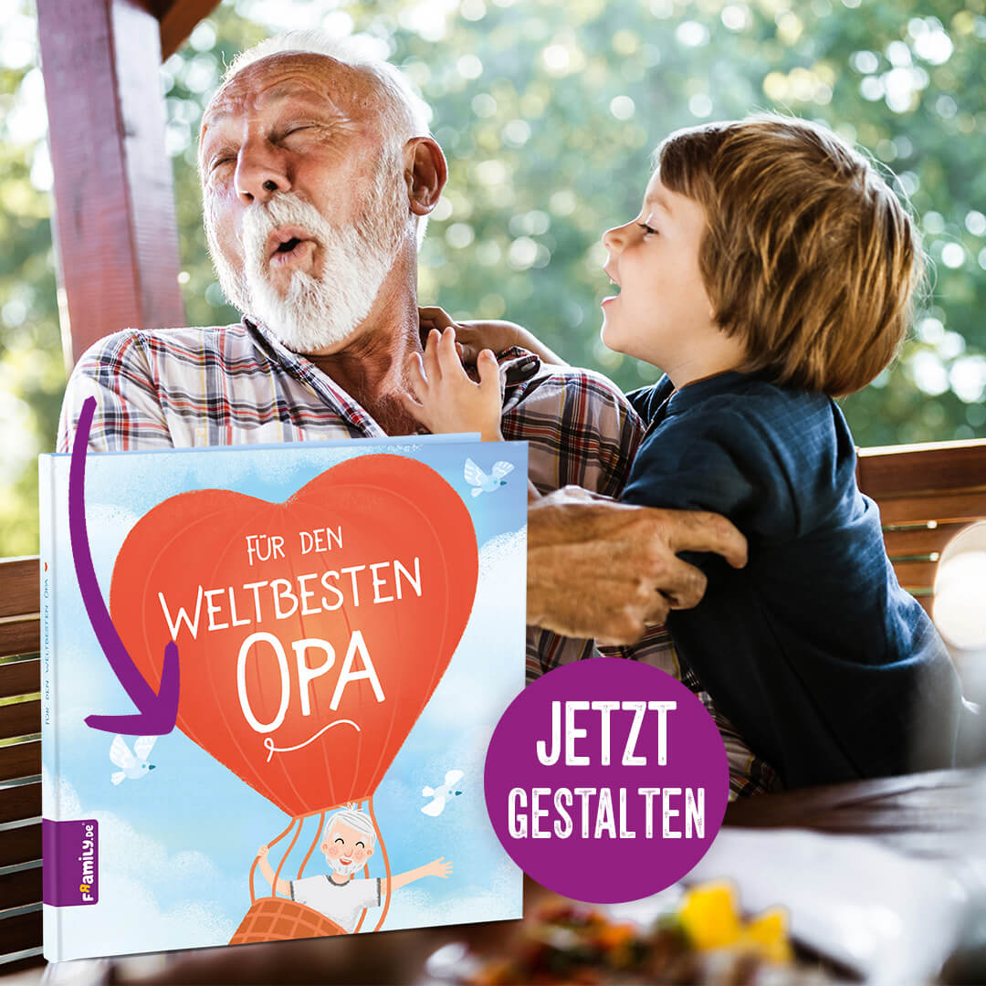 Ein lachender älterer Mann sitzt im Freien an einem Tisch, und ein lächelnder kleiner Junge umarmt ihn. Im Vordergrund ist ein großer illustrierter Bucheinband zu sehen, der einen roten Heißluftballon und die Worte Für den weltbesten Opa zeigt.