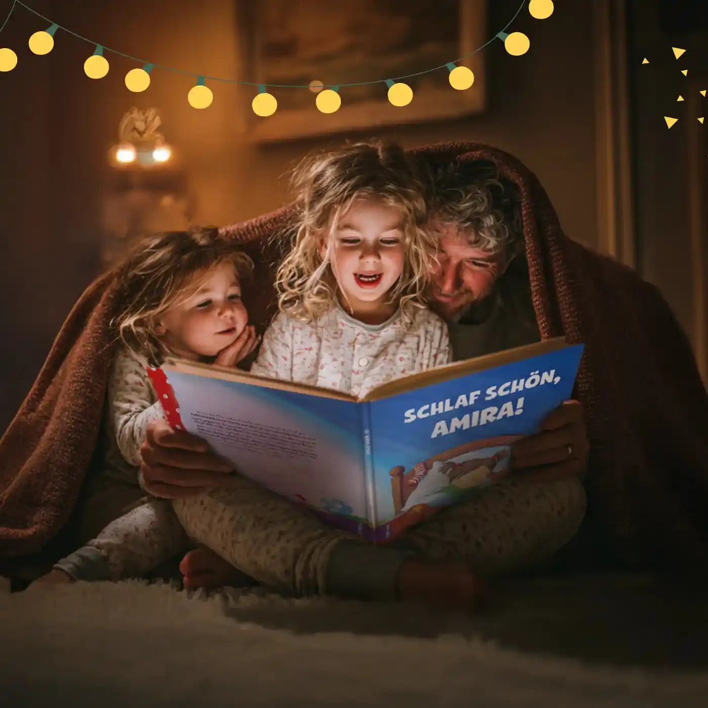 Vater sitzt mit beiden Töchtern unter Kuscheldecke im Wohnzimmer und liest aus dem personalisierten Gute-Nacht-Buch vor